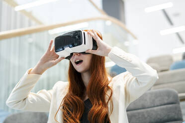 Businesswoman with mouth open looking through virtual reality simulator in office - SSGF00450