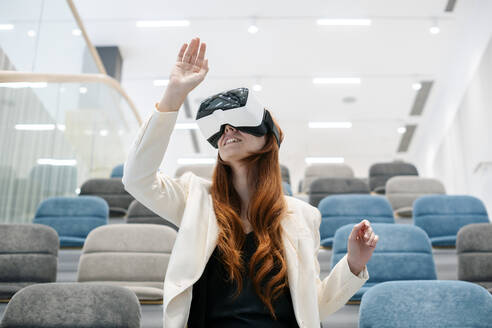 Rothaarige berufstätige Frau mit Virtual-Reality-Headset gestikuliert im Büro - SSGF00454