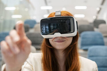 Smiling businesswoman wearing virtual reality headset gesturing in office - SSGF00458