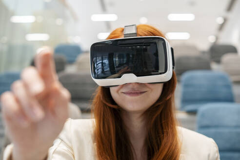 Lächelnde Geschäftsfrau mit Virtual-Reality-Headset gestikuliert im Büro - SSGF00458