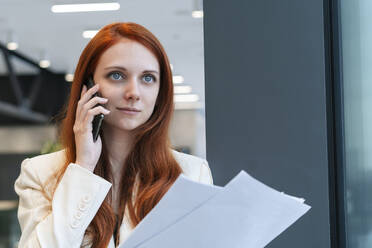 Arbeitende Frau, die Dokumente in der Hand hält und über ein Smartphone diskutiert - SSGF00467