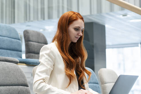 Arbeitende rothaarige Frau mit Laptop in einem Hörsaal im Büro sitzend - SSGF00483