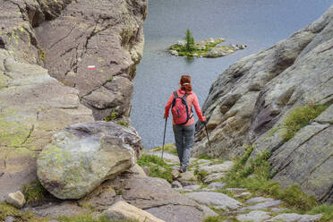 Woman with backpack and hiking poles walking towards Lac Fourca lake, Maritime Alps, Mercantour National Park, France - ANSF00145