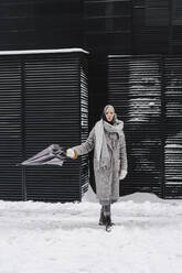 Selbstbewusste Frau im Mantel mit Regenschirm auf verschneitem Fußweg - SEAF00358