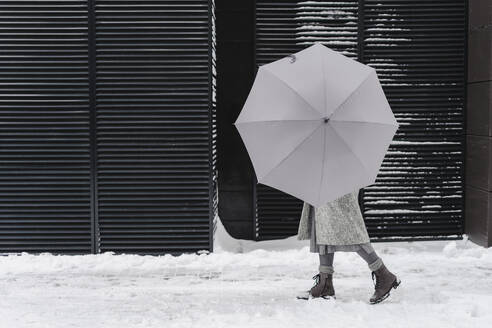 Frau mit offenem Regenschirm auf verschneitem Fußweg - SEAF00359