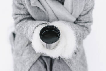 Woman wearing fur gloves holding water in insulated cup - SEAF00391