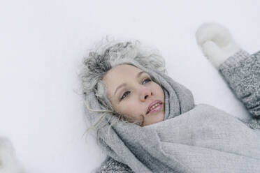 Kontemplative Frau mit grauem Schal im Schnee liegend - SEAF00393