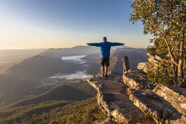 Australien, Victoria, Halls Gap, Männlicher Tourist steht mit ausgestreckten Armen am Rand des Boroka Lookout in der Morgendämmerung - FOF12669