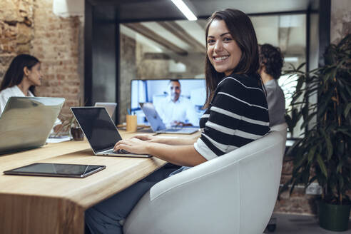Smiling businesswoman with laptop in meeting at coworking office - JSRF01800