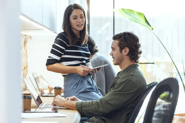 Businessman and businesswoman discussing while working in coworking office - JSRF01802