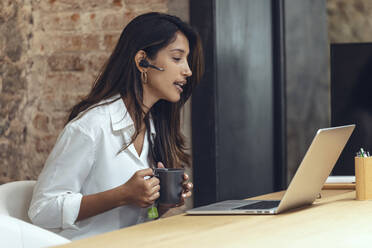 Businesswoman with coffee mug discussing on video call in coworking office - JSRF01805