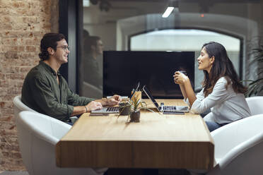 Geschäftsmann und Geschäftsfrau mit Laptops, die am Schreibtisch in einem Coworking-Büro diskutieren - JSRF01806