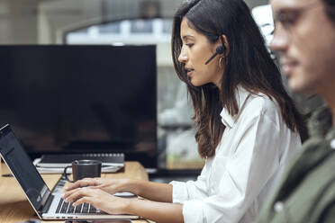 Junge Geschäftsfrau mit Laptop bei einem Geschäftsmann am Schreibtisch in einem Coworking-Büro - JSRF01812