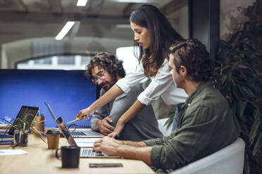 Businesswoman explaining business strategy to colleagues on laptop in meeting at office - JSRF01820