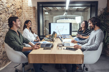 Smiling businessmen and businesswomen sitting at conference table in coworking office - JSRF01824