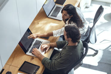 Businessman and businesswoman discussing over laptop at desk in coworking office - JSRF01831