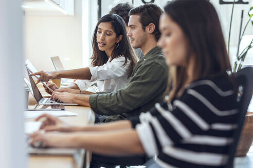 Geschäftsfrau erklärt Geschäftsmann über Laptop am Schreibtisch im Coworking-Büro - JSRF01833