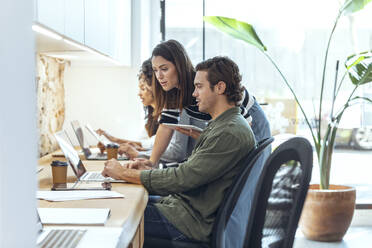 Geschäftsmann erklärt Geschäftsfrau über Laptop am Schreibtisch im Coworking-Büro - JSRF01837