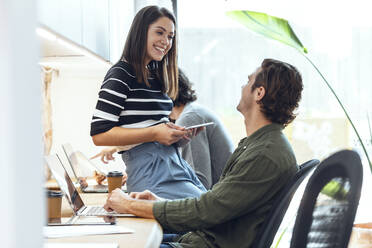 Lächelnde Geschäftsfrau im Gespräch mit Geschäftsmann in Coworking-Büro - JSRF01838