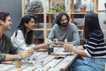 Happy businessmen and businesswomen having burritos at office cafeteria - JSRF01846