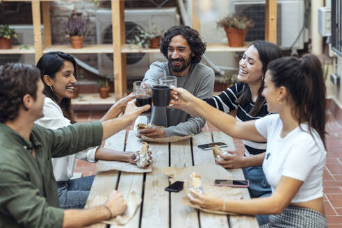 Happy businessmen and businesswomen toasting drinks at cafeteria - JSRF01849