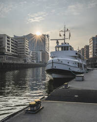 Germany, Hamburg, Boat moored in Sandtorhafen canal with sun setting over Elbphilharmonie in background - KEBF02122