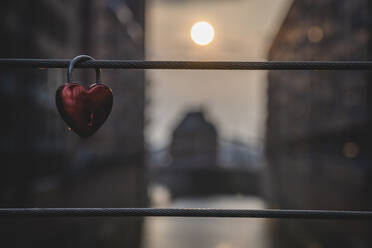 Love lock hanging on bridge railing with setting sun in background - KEBF02123