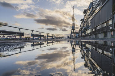 Germany, Hamburg, Harbor crane reflecting in puddle of water at dusk - KEBF02184