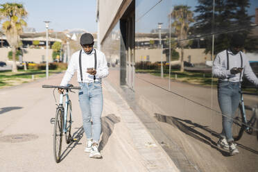 Junger Mann mit Smartphone und Fahrrad auf dem Gehweg - JCZF00942