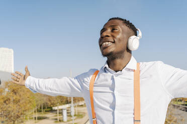 Glücklicher Mann, der an einem sonnigen Tag über Kopfhörer Musik hört - JCZF00950