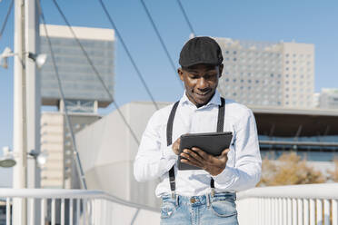 Smiling man using tablet PC on bridge in city - JCZF00953