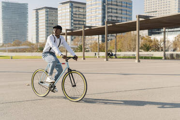 Junger Mann mit Mütze beim Radfahren an einem sonnigen Tag in der Stadt - JCZF00958