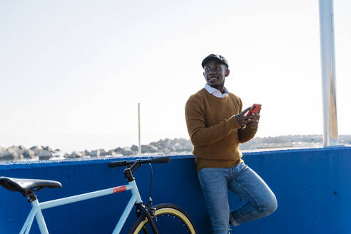 Nachdenklicher Mann mit Smartphone und Fahrrad in der Stadt - JCZF00963