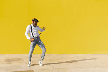 Man wearing suspenders dancing in front of yellow wall - JCZF00968