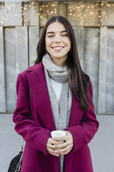 Lächelnde schöne junge Frau im Wintermantel mit Einwegbecher - JRVF02486
