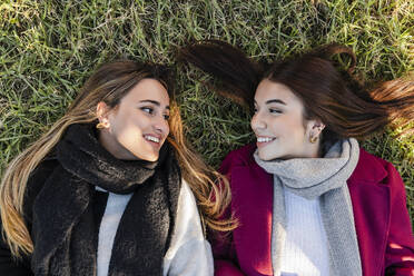 Lächelnde Frauen, die sich im Gras liegend anschauen - JRVF02491