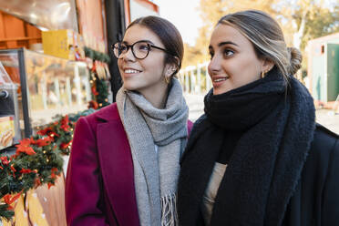 Lächelnde Freunde in warmer Kleidung vor einem Schaufenster - JRVF02498