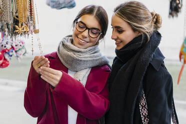 Lächelnde junge Freunde betrachten einen Rosenkranz auf dem Markt - JRVF02499