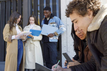 Studenten bei der Nutzung eines Tablet-PCs mit Freunden, die im Hintergrund auf dem Universitätscampus lernen - IFRF01397