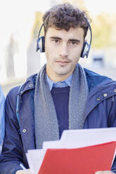 Young man listening music through headphones on university campus - IFRF01413