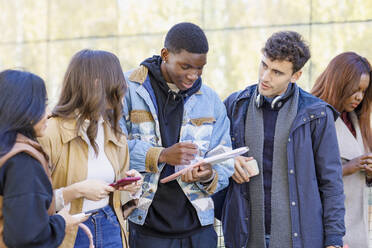 Gemischtrassige Freunde diskutieren über ein Buch auf dem Campus - IFRF01418