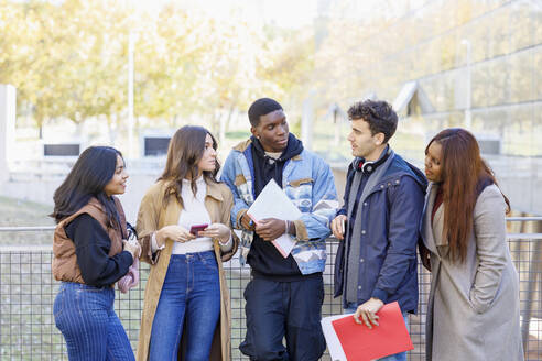Gemischtrassige Studenten unterhalten sich an einem Geländer auf dem Universitätscampus - IFRF01419