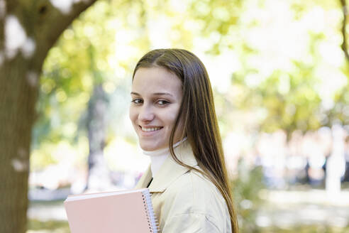 Lächelnde Frau mit Buch im College Park - IFRF01474