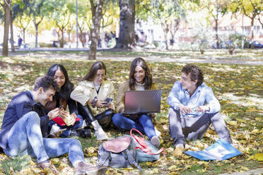 Happy students using smart phone and laptop in college park - IFRF01487