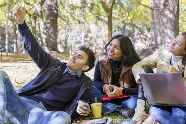 Smiling man taking selfie with friends on smart phone in college park - IFRF01491