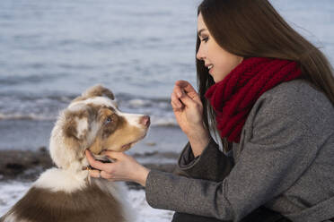 Junge Frau streichelt Hund am Strand - SSGF00500