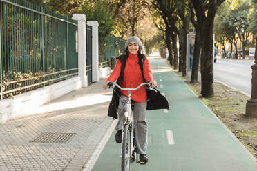 Smiling young woman cycling on bicycle lane - JRVF02510