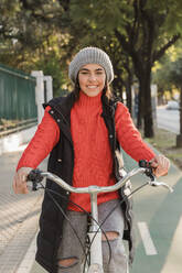 Lächelnde junge Frau beim Radfahren auf dem Radweg - JRVF02513
