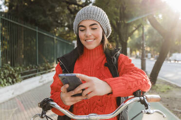 Happy woman with bicycle using mobile phone - JRVF02515