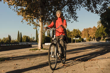 Cheerful young woman cycling on footpath - JRVF02519